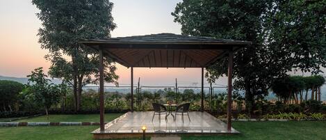 A gazebo with a table and chairs, surrounded by a well-maintained lawn and trees, overlooking a scenic view.