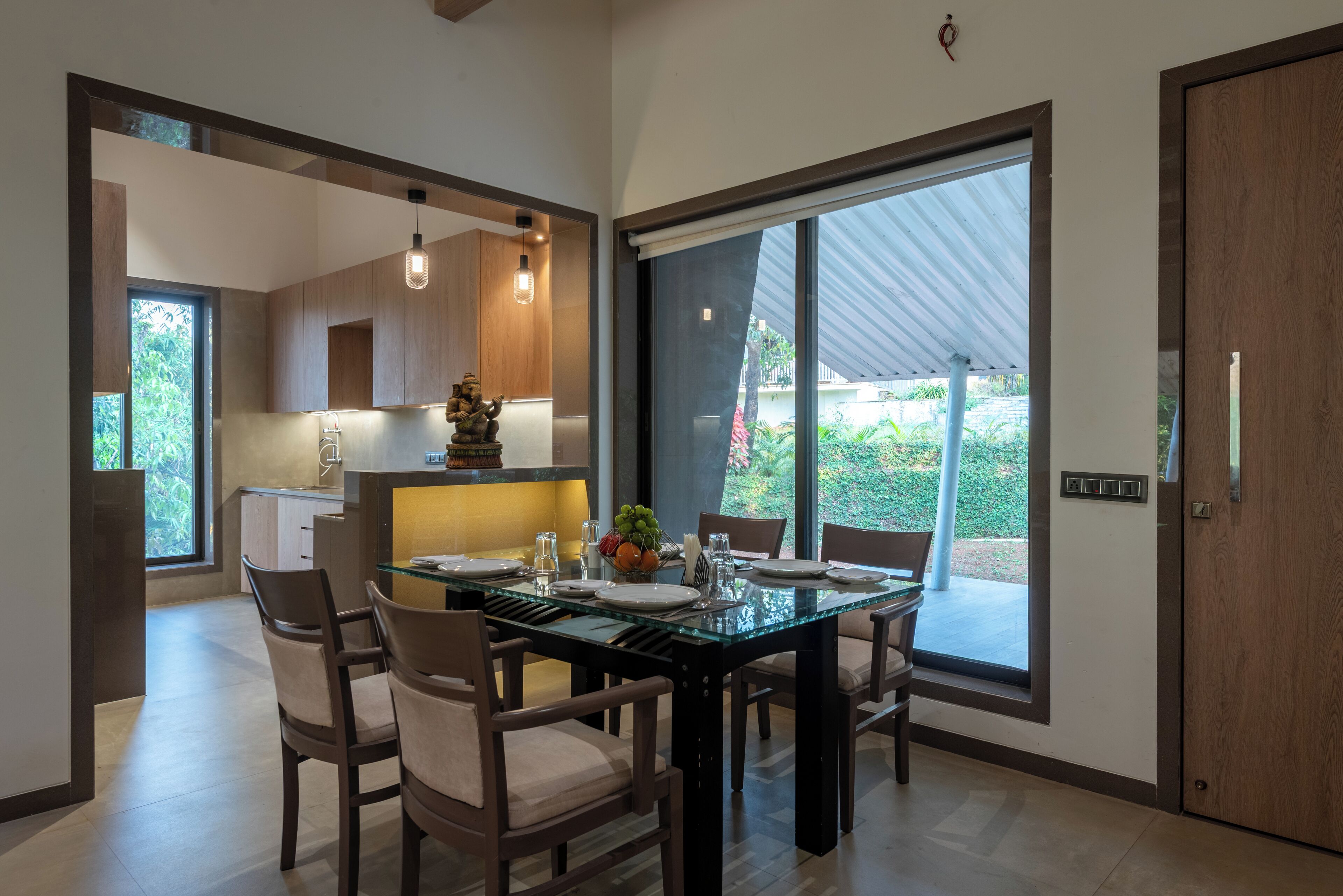 A modern dining area with a glass table, wooden chairs, and a view of the outdoors.