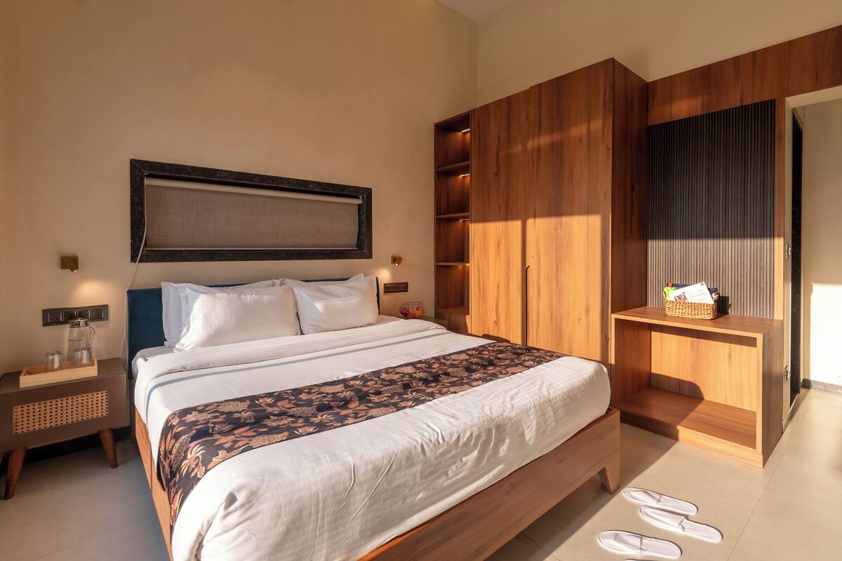 A modern bedroom with a large bed, wooden wardrobe, bedside tables, and a small desk with a basket.