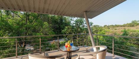 Un balcón con mesa y sillas, con vista a un paisaje verde exuberante.
