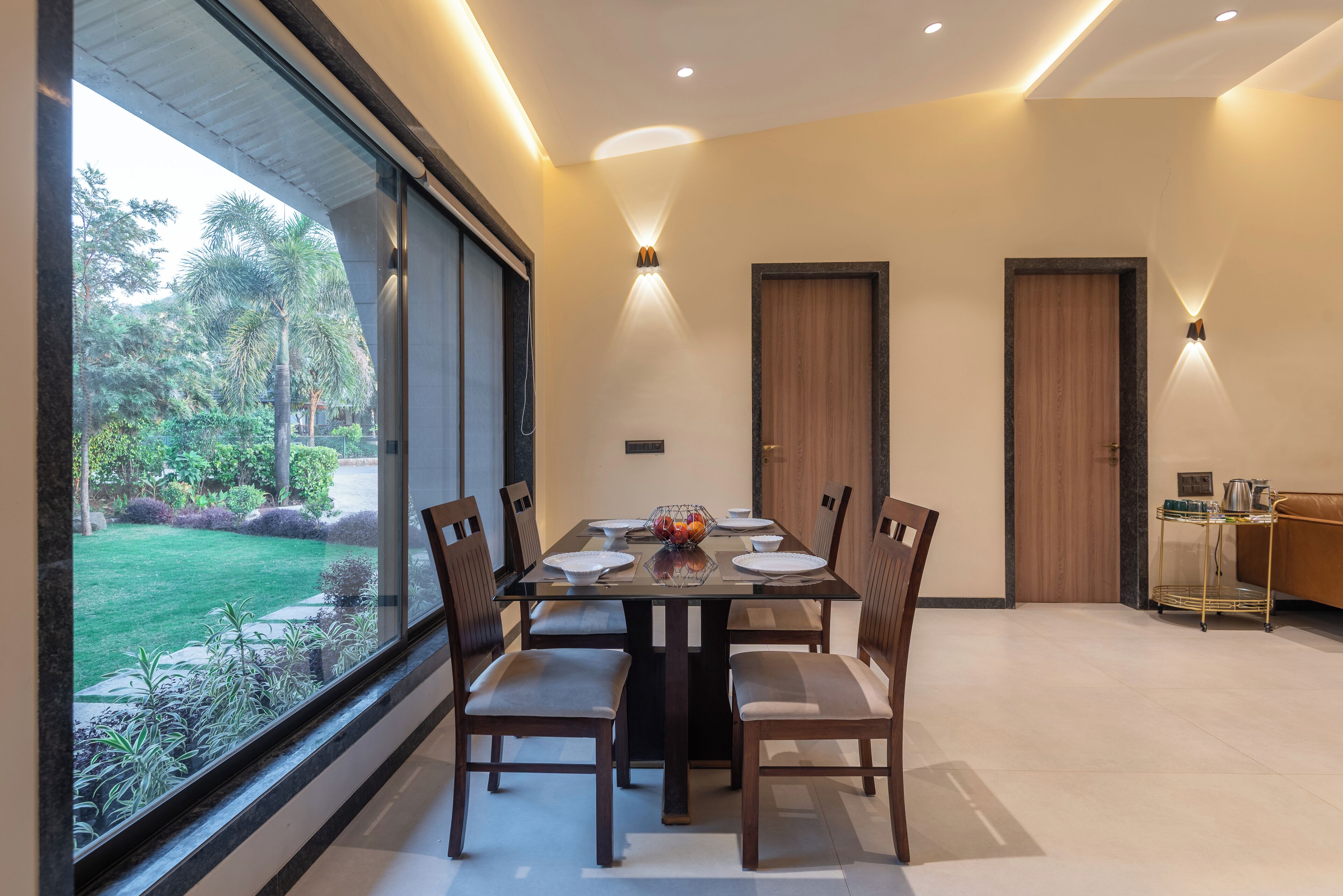 Un comedor con una mesa de vidrio, sillas de madera y vistas a un jardín a través de amplios ventanales.