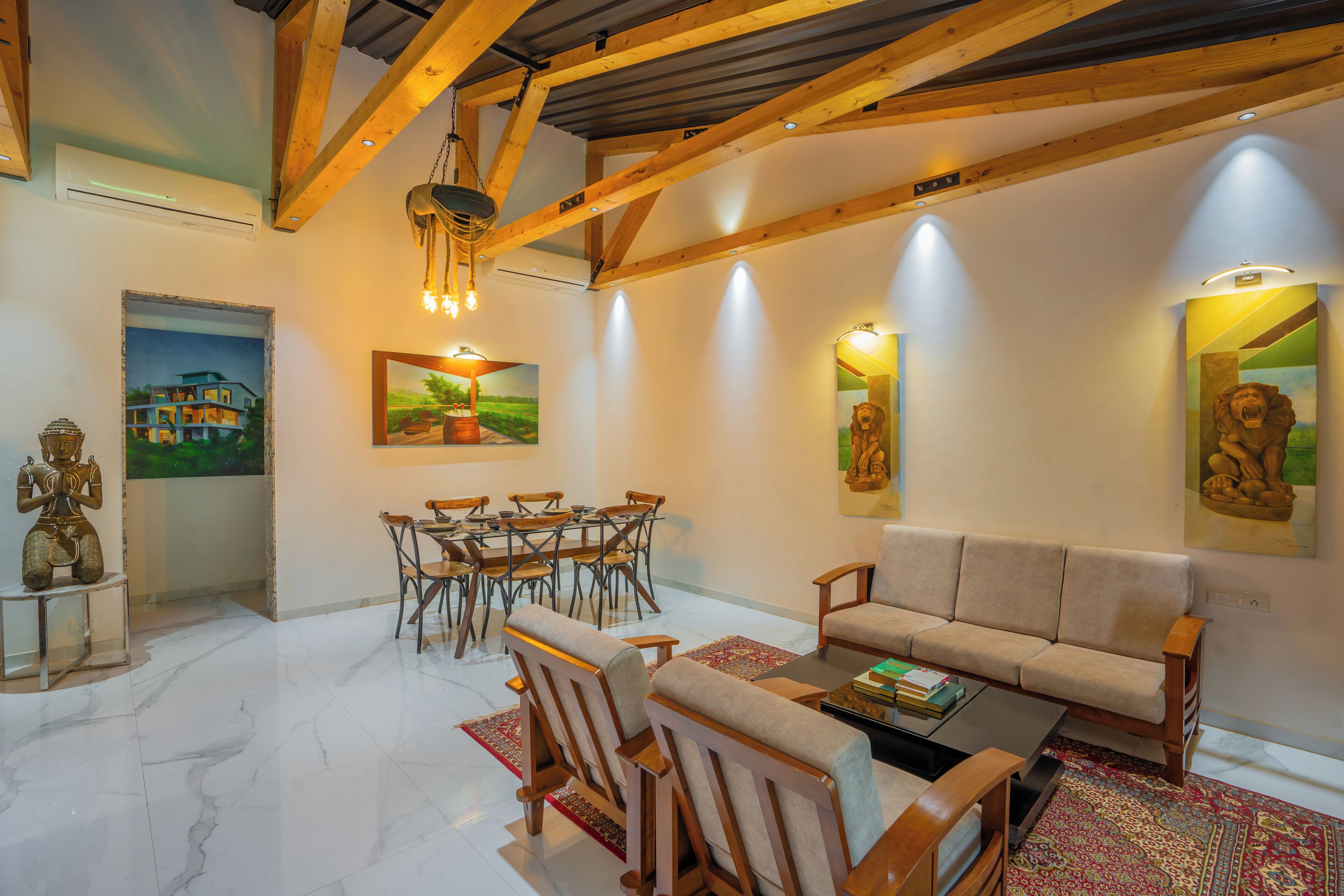 A spacious living room with a high ceiling, wooden beams, a sofa, a coffee table, a dining area with chairs, and artwork on the walls.