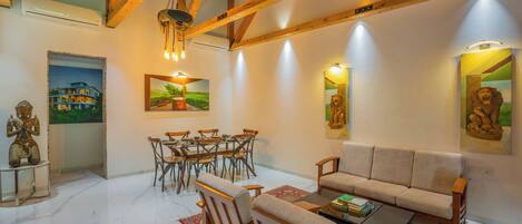 Ein geräumiges Wohnzimmer mit hohen Decken, Holzbalken, einer Couch, einem Couchtisch, einem Essbereich mit Stühlen und Kunstwerken an den Wänden.