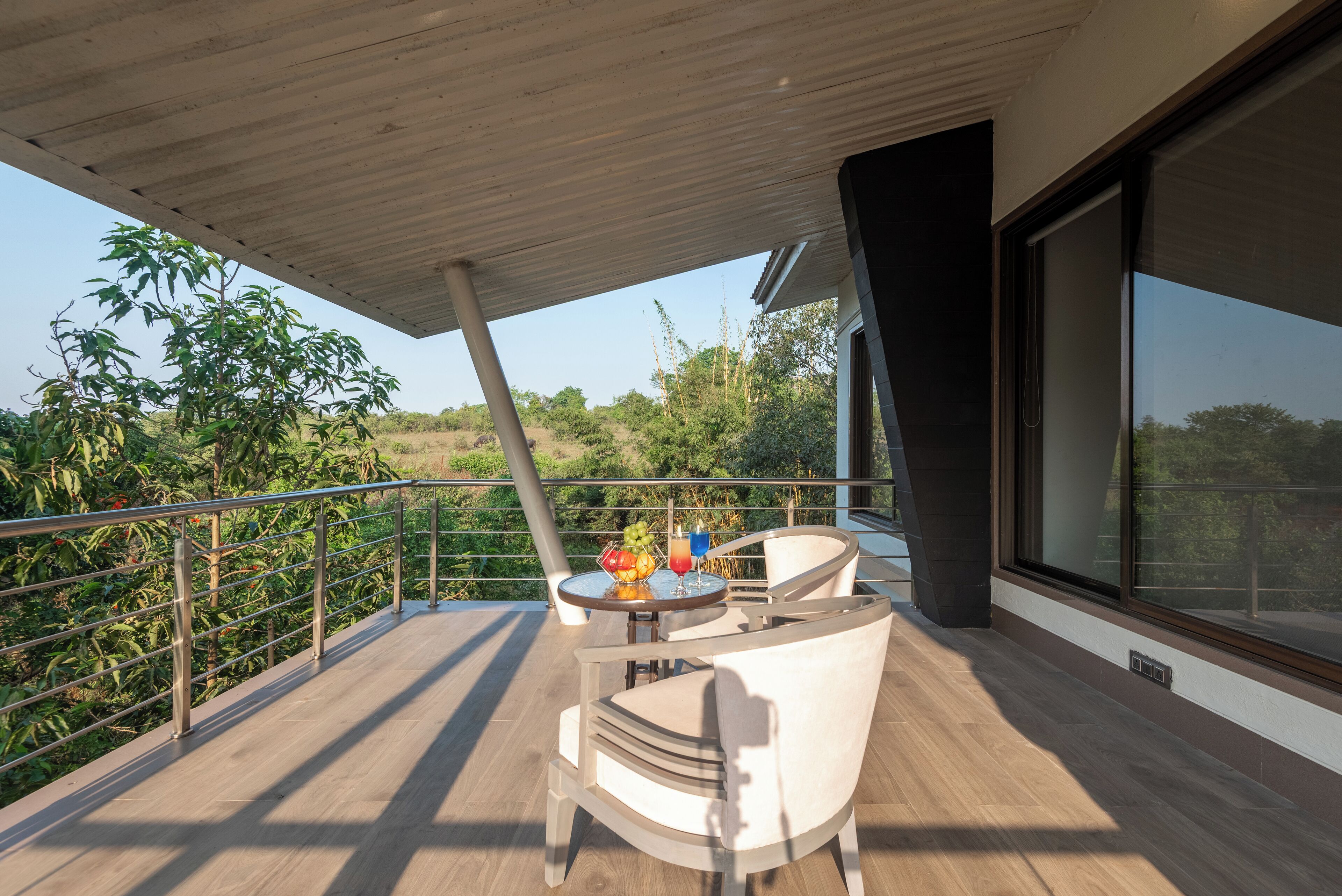 Ein moderner Balkon im Freien mit Holzboden, einem Glastisch mit Früchten und Getränken und einem weißen Stuhl.