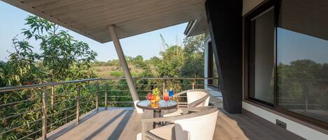 A modern outdoor balcony with a wooden ceiling, a glass table with fruit and drinks, and a white chair.