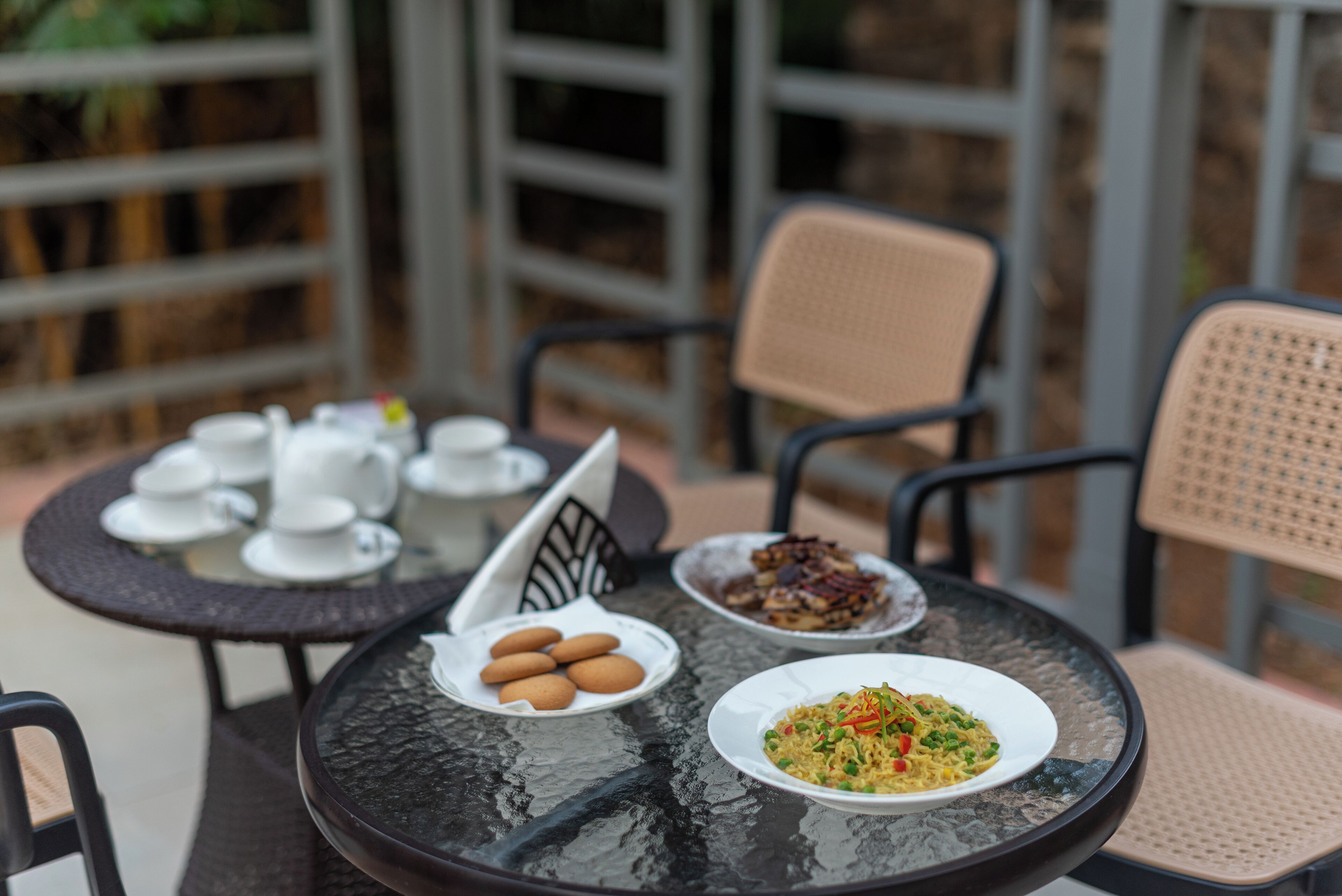 A round glass table with plates of food, cups, and a teapot.