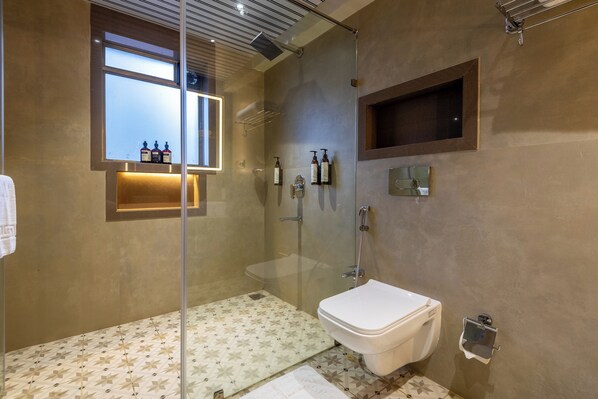 Un baño moderno con ducha de vidrio, inodoro y estante con artículos de tocador.