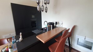 A modern kitchen with a black countertop, wooden bar counter, and red bar stools. - 3-Apartment Coastal Italian Villa (San Lorenzo - Civezza)