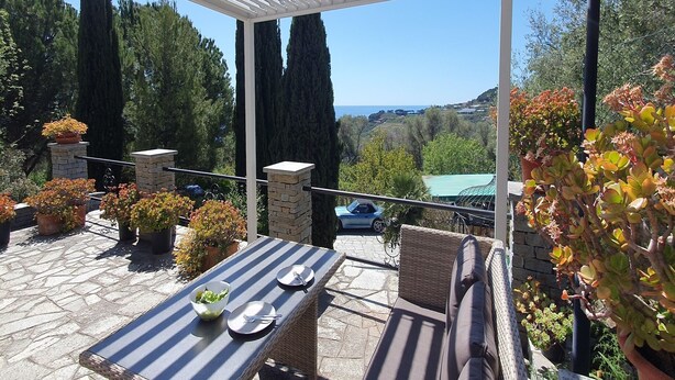 An outdoor patio with a table set for dining, surrounded by potted plants and a view of the sea. - 3-Apartment Coastal Italian Villa (San Lorenzo - Civezza)