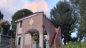 A brick building with a central archway, stone pillars, and a small garden area with potted plants. - 3-Apartment Coastal Italian Villa (San Lorenzo - Civezza)
