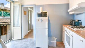 Eine kompakte Küche mit Kühlschrank, Mikrowelle, Herd und einer kleinen Mülltonne.