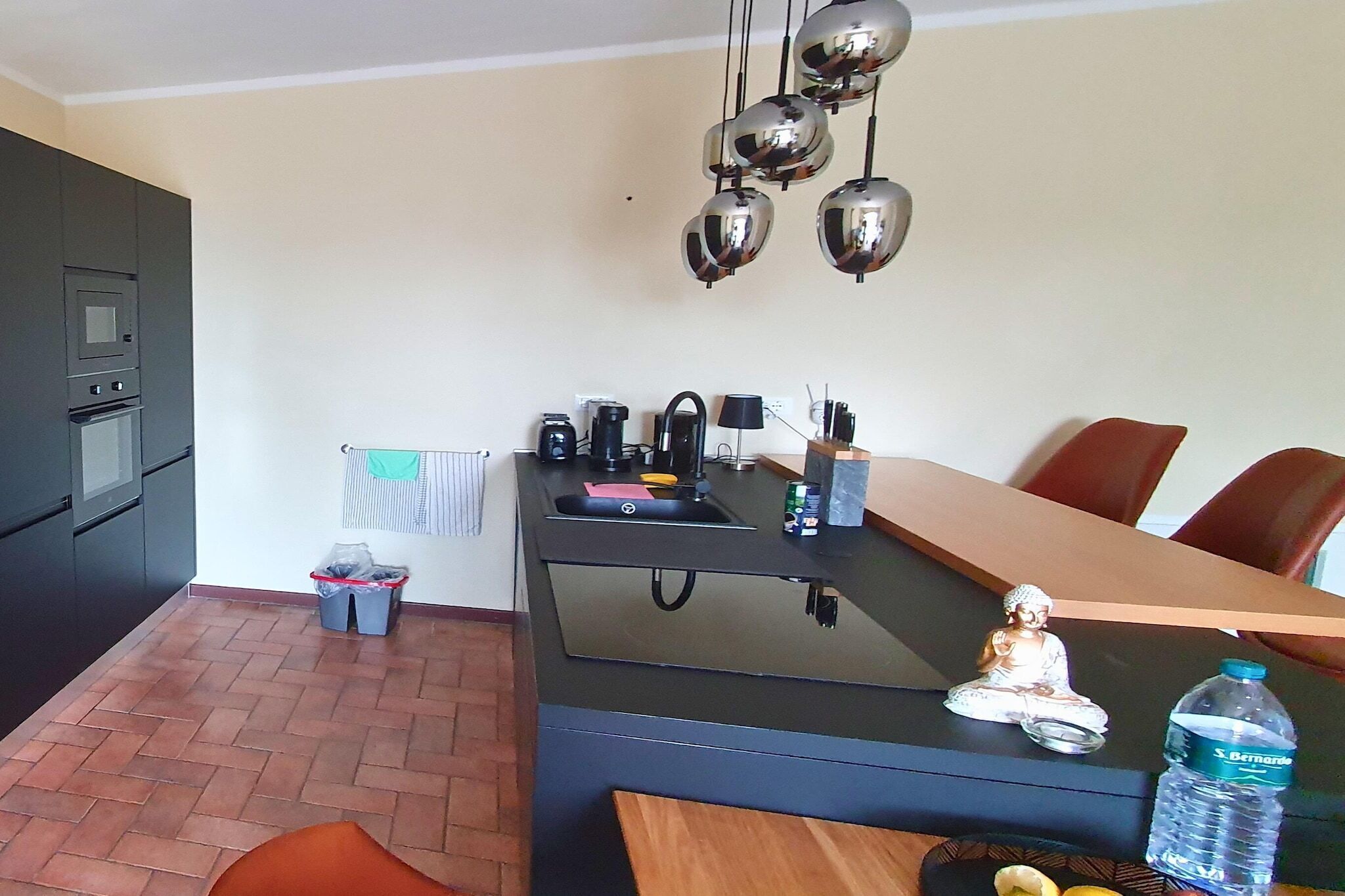 A modern kitchen with a central island, a built-in oven, and a hanging light fixture.