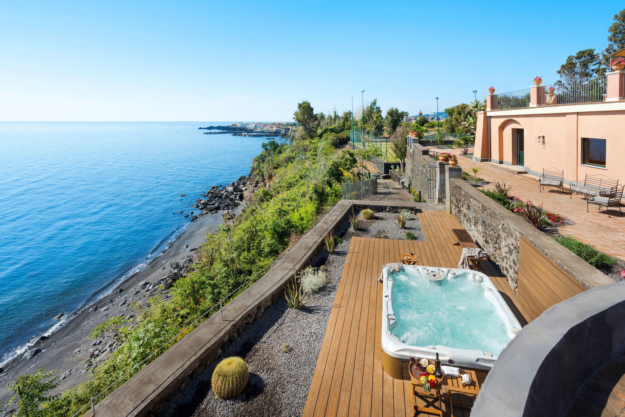 A coastal property with a wooden deck, a hot tub, and a view of the sea.
