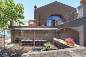 A two-story building with a covered patio area, outdoor seating, and a view of the sea. - Sea front villa with pool and tennis court - DiCasaInSicilia (Pozzillo)