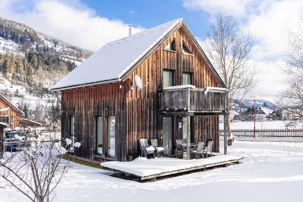 A wooden cabin with a balcony, surrounded by snow-covered landscape.