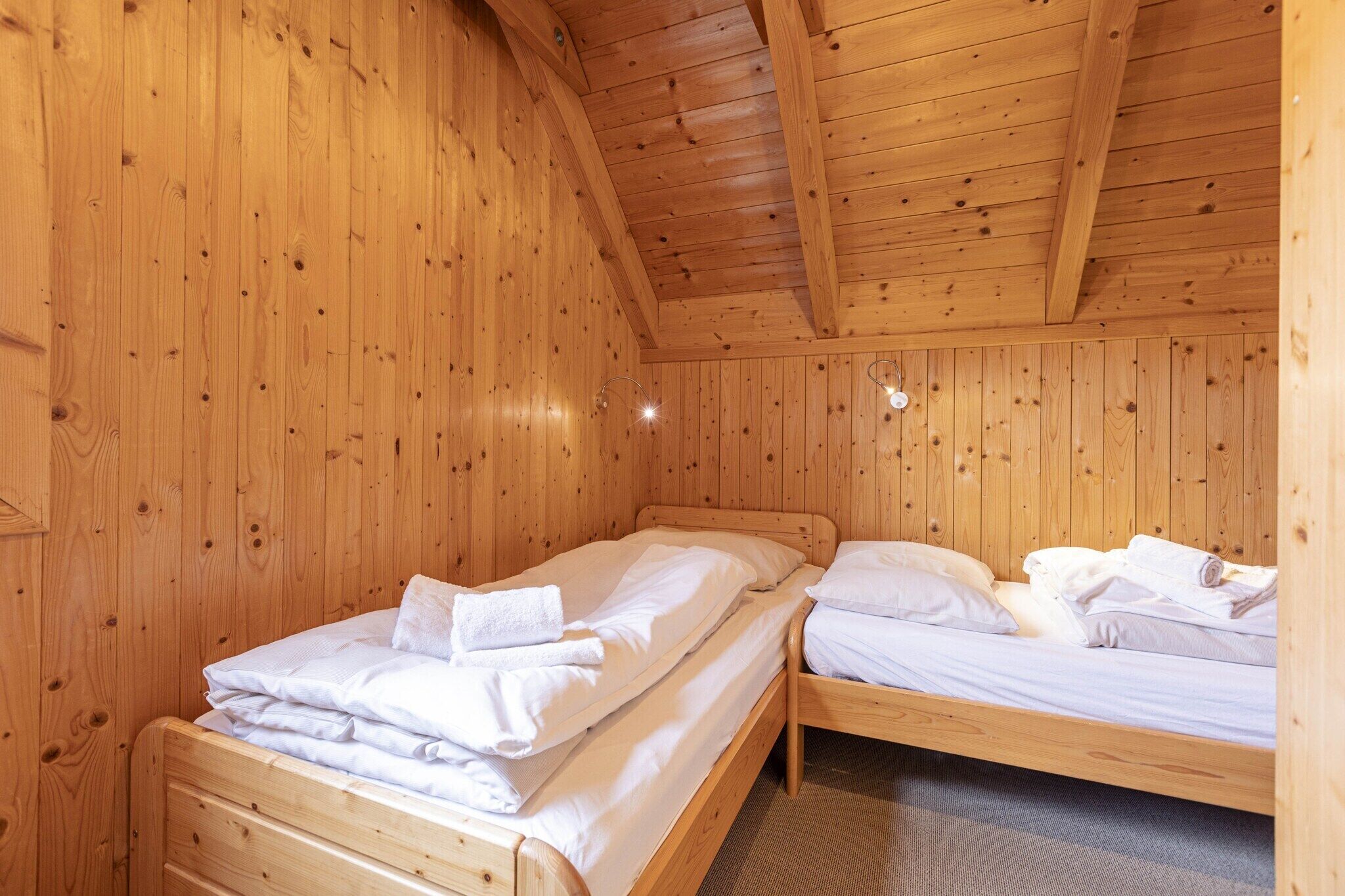 A wooden cabin room with two beds, each with neatly made white linens and towels.