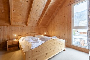 Ein Schlafzimmer einer Holzhütte mit einem Einzelbett, einem Nachttisch, einer Lampe und einem großen Fenster mit Blick auf einen Berg und Gebäude.
