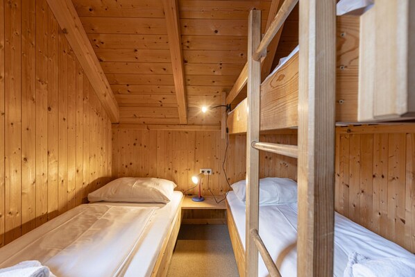 Ein Holzhütten-Zimmer mit Etagenbetten, einem kleinen Tisch mit Lampe und einem Fenster.