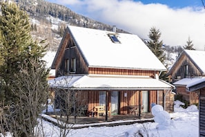 Eine Holzhütte mit verschneitem Dach, einer Terrasse und einem großen Schneemann.