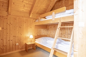 Une chambre dans un chalet en bois, avec des lits superposés, une petite table de chevet avec une lampe et une échelle.