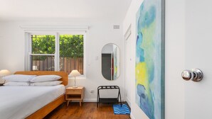 Un dormitorio con una cama de madera, una mesita de noche, un espejo y un cuadro abstracto azul en la pared.