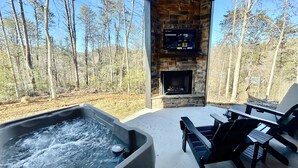 Pejs af sten med et tv ovenover, jacuzzi og udendørs møbler.