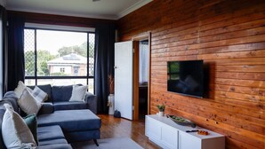 A modern living room with a sectional sofa, a flat-screen TV mounted on a wooden wall, and a sliding glass door leading to a balcony.