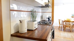 A kitchen with white cabinets, a wooden countertop, a toaster, a kettle, a stove, and a dining area with a table and chairs.