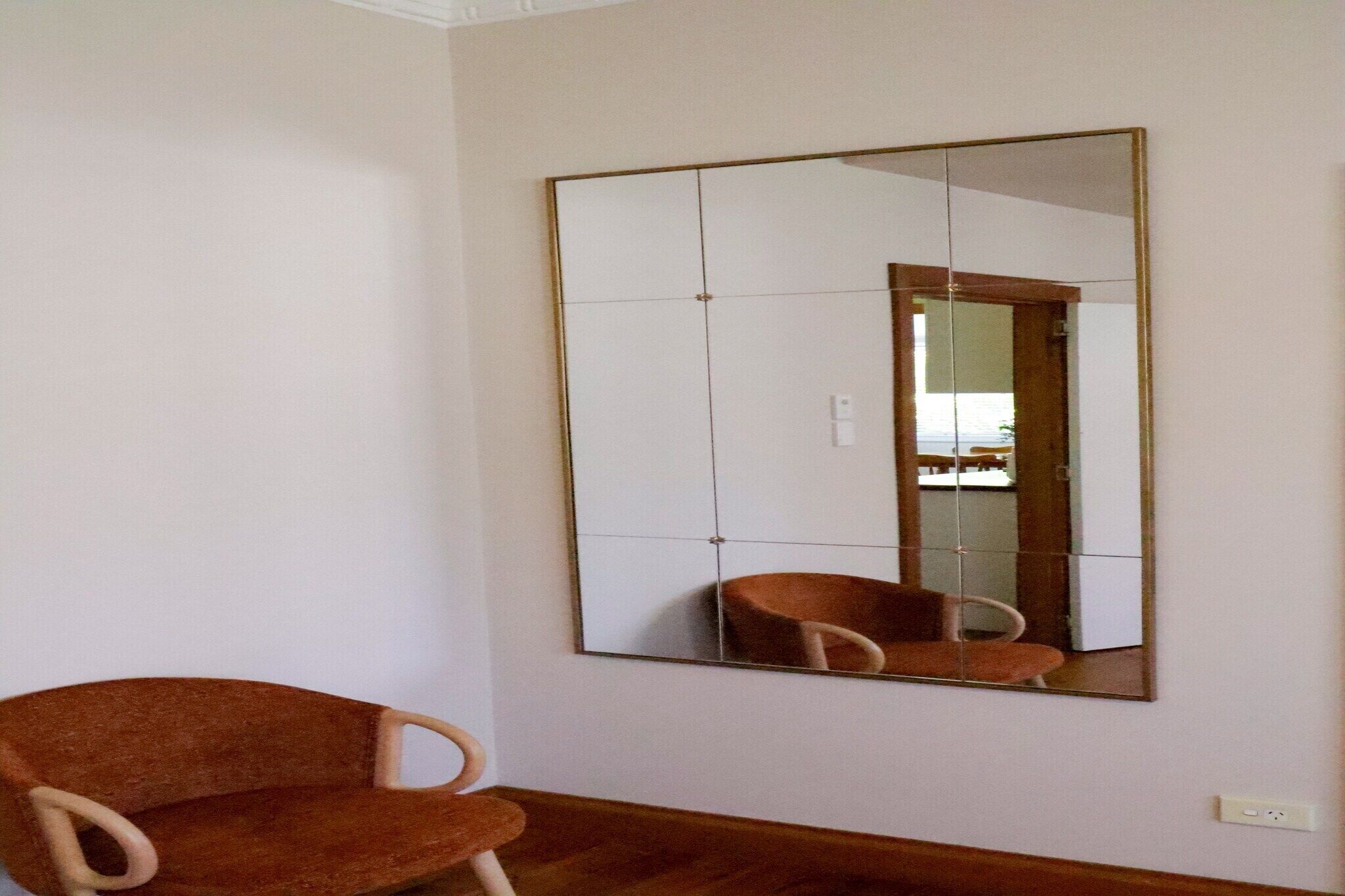 A room with a large mirror on the wall, a wooden floor, and a brown chair.