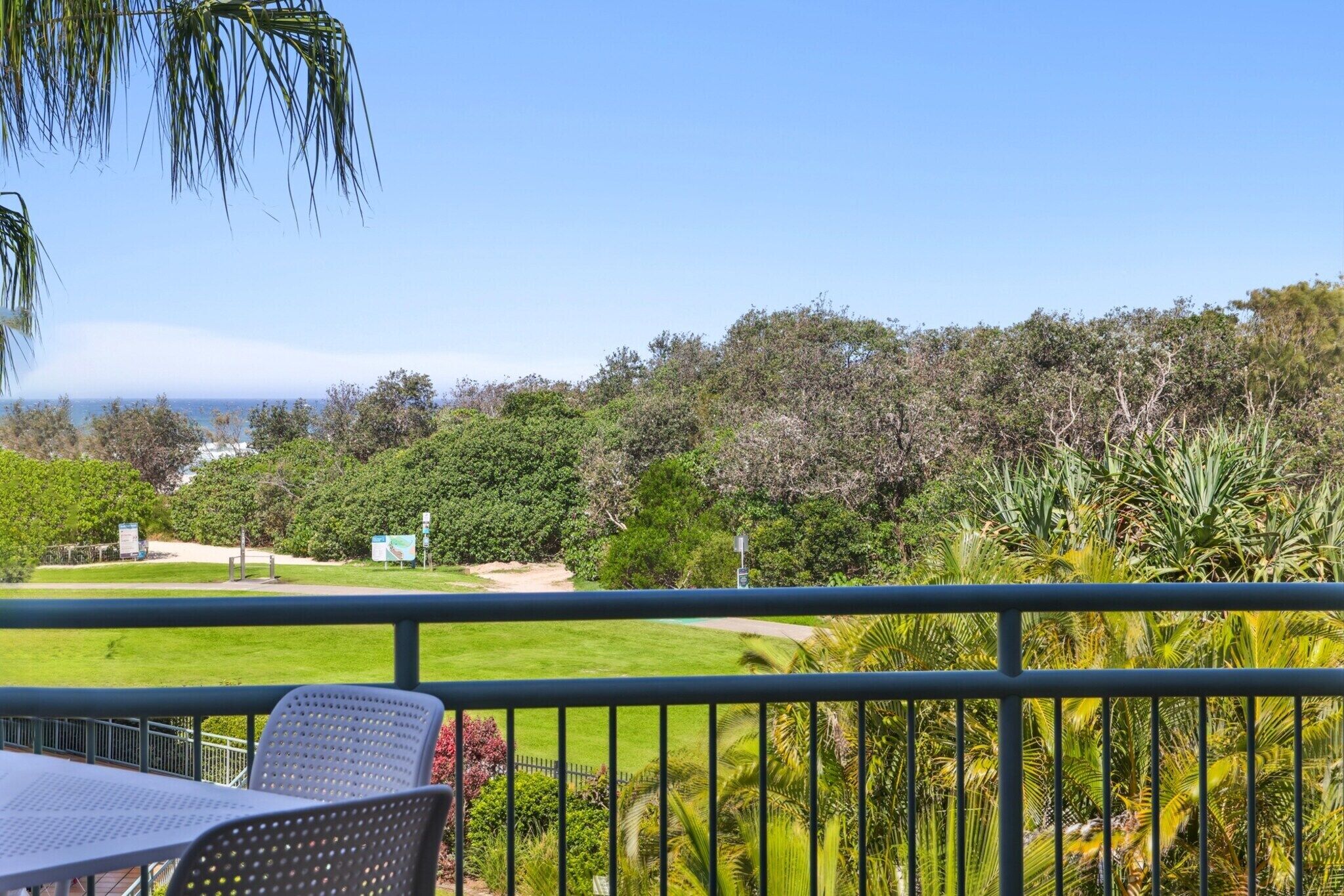 A balcony with a view of a lush garden and a distant body of water.