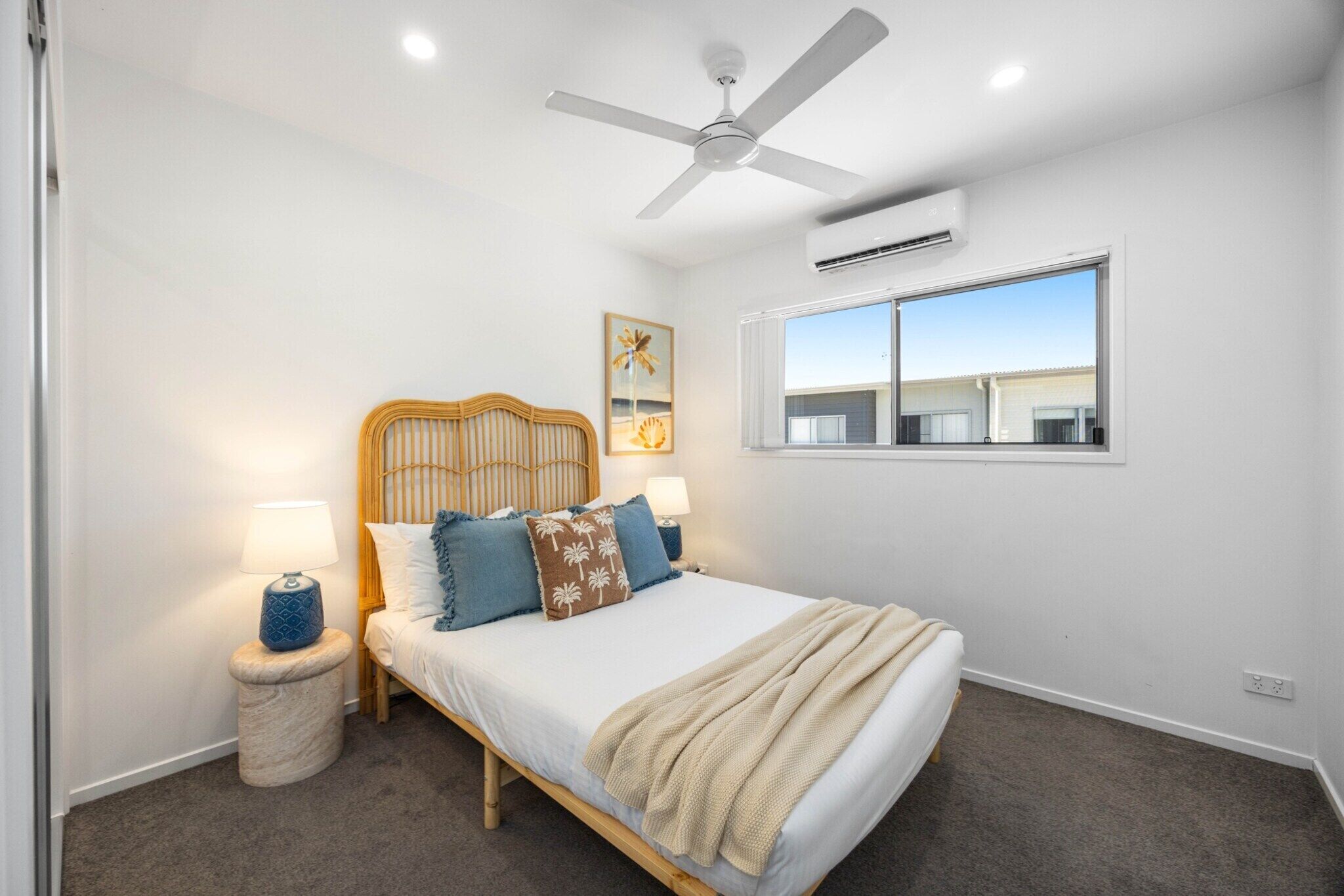 Une chambre à coucher comprenant un lit, un ventilateur de plafond, un appareil de climatisation, une fenêtre et une table de chevet avec une lampe.