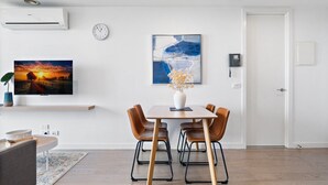Un soggiorno moderno con un tavolo da pranzo in legno, poltrone in pelle marrone, una TV a schermo piatto montata a parete e un grande quadro astratto.