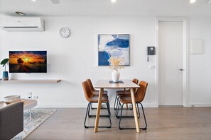 Ein modernes Wohnzimmer mit einem Holzesstisch, braunen Ledersesseln, einem wandmontierten Flachbildfernseher und einem großen abstrakten Gemälde.