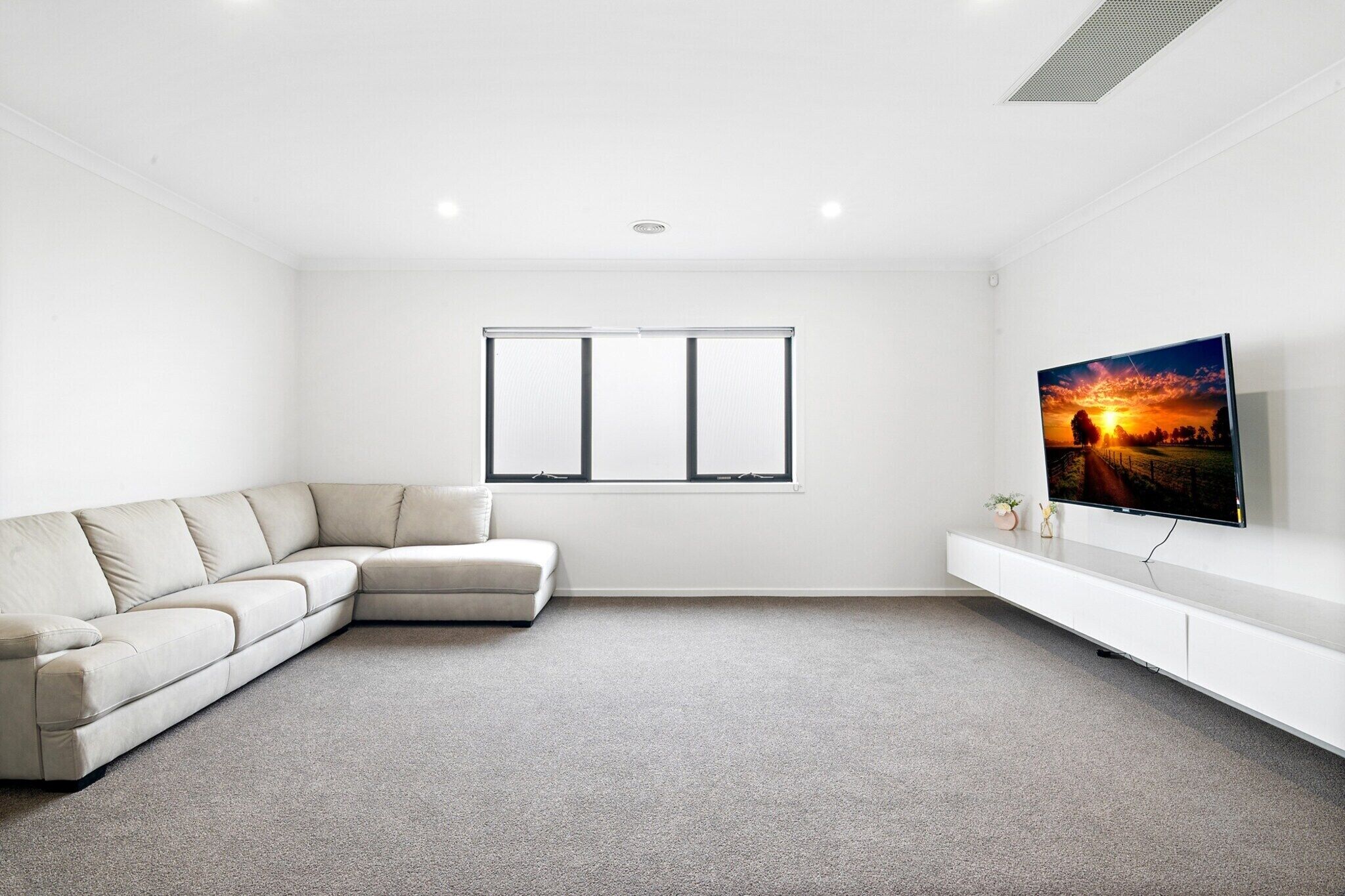 Un salon moderne avec un canapé d’angle, un téléviseur à écran plat et une grande fenêtre.