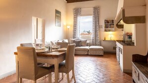 Un rincón comedor acogedor con una mesa y sillas de madera, un sofá con cojines, y una zona de cocina con mostrador y estanterías.