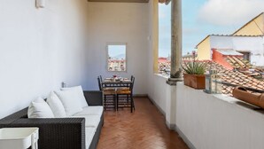 Un balcón con un sofá de mimbre, una mesa de comedor con sillas y plantas en macetas.