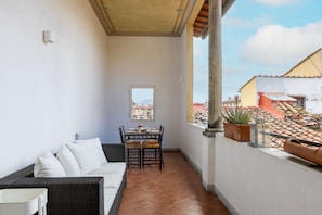 A balcony with a wicker sofa, a dining table with chairs, and potted plants. - Duomo Sky Terrace Apartment (Florence)