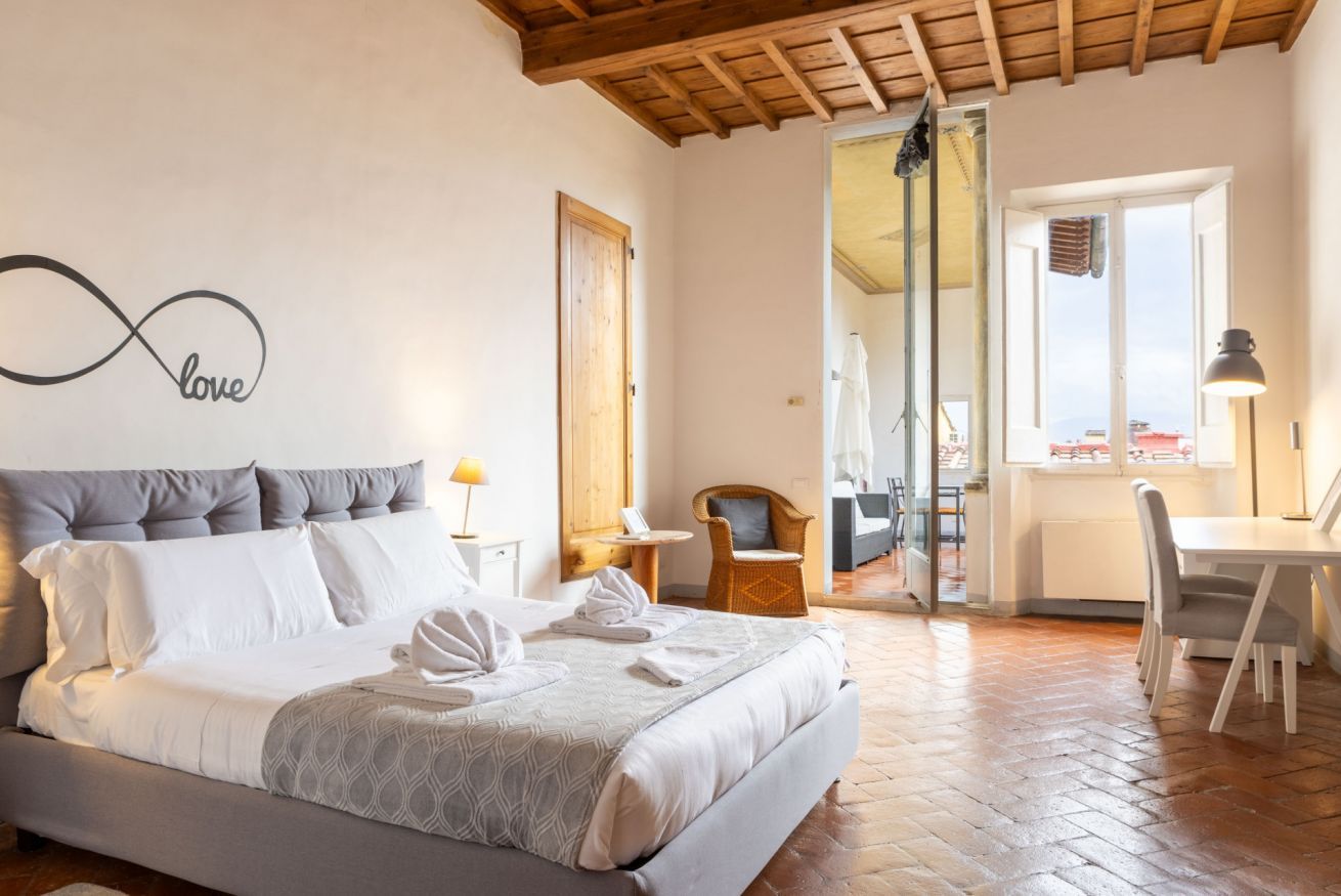 Een slaapkamer met een bed, een muur met een 'love' oneindigheidsymbool, een zithoek met een tafel en stoelen, en uitzicht door een glazen deur.