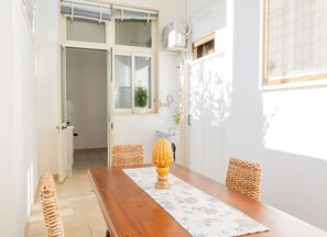 A room with a wooden dining table, wicker chairs, a window with blinds, and a potted plant.