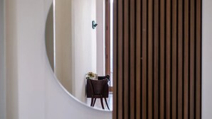Une pièce dans laquelle on trouve un miroir rond qui reflète une chaise et une petite table ornée de fleurs.