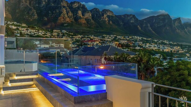 A rooftop pool with a glass barrier, overlooking a cityscape with mountains in the background. - Luxury villa 120m from beach & restaurants striking ocean & mountain view-by JGM (Cape Town)