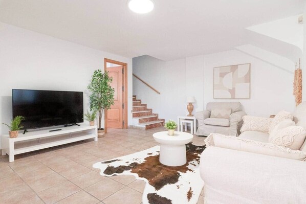 A living room with a TV, a sofa, a coffee table, a staircase, and a door. - House with Barbecue Pool and Private Parking - Zona norte playa Gandía (Gandia)