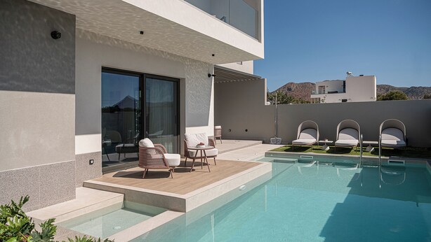 Uma área de piscina moderna com piscina transparente, mobiliário de exterior e vista para a paisagem circundante.