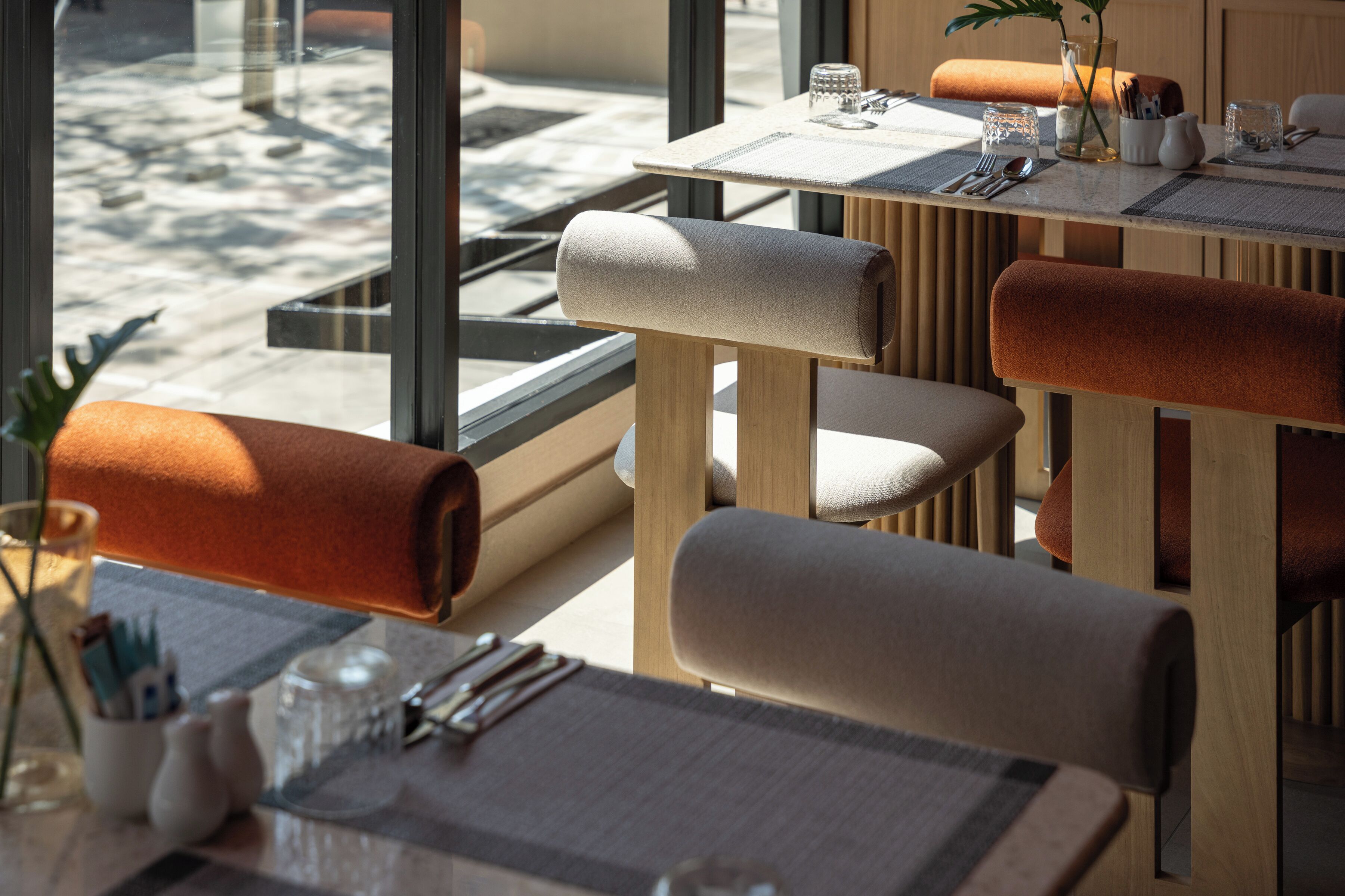 A modern dining area with wooden tables and chairs, clear glassware, and a view of the outdoors.
