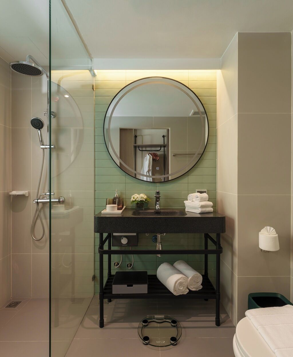 A modern bathroom with a glass shower enclosure, a round mirror, a black vanity with a sink, and a towel rack.