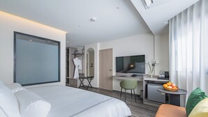 Une chambre d’hôtel moderne équipée d’un lit, d’un bureau, d’une télévision et d’une petite table sur laquelle se trouvent des fruits.