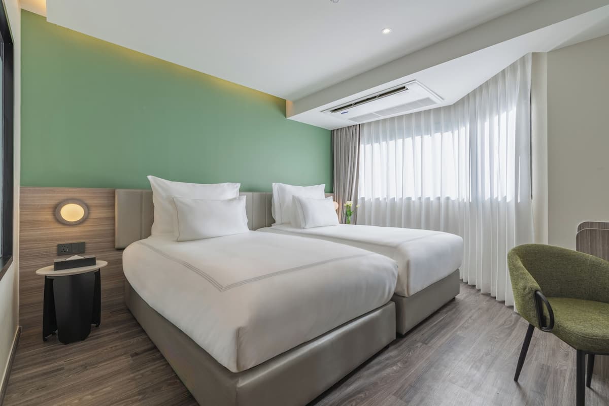 A hotel room with two beds, a small table, a chair, and a large window with curtains.