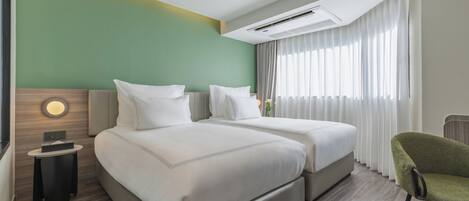 Habitación de hotel con dos camas, una mesita, una silla y un amplio ventanal con cortinas.