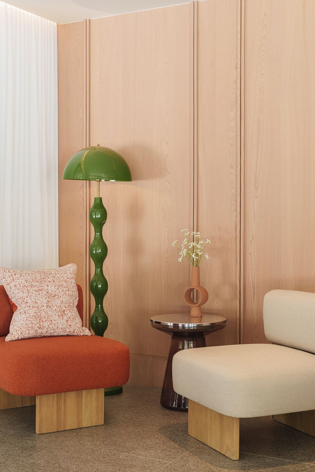 Une pièce comprenant un canapé, un fauteuil, un lampadaire vert, une petite table avec un vase de fleurs et des murs recouverts de panneaux en bois.