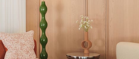 A room with a sofa, a chair, a green floor lamp, a small table with a vase of flowers, and wooden panel walls.